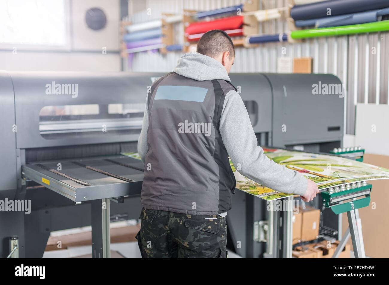Technician worker operator works on large premium industrial printer ...