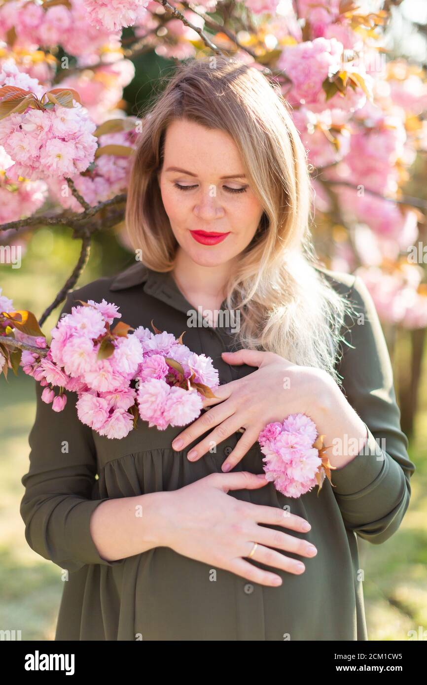 Freckled Blonde Pregnant Woman In The Park At Spring With Sakura Trees