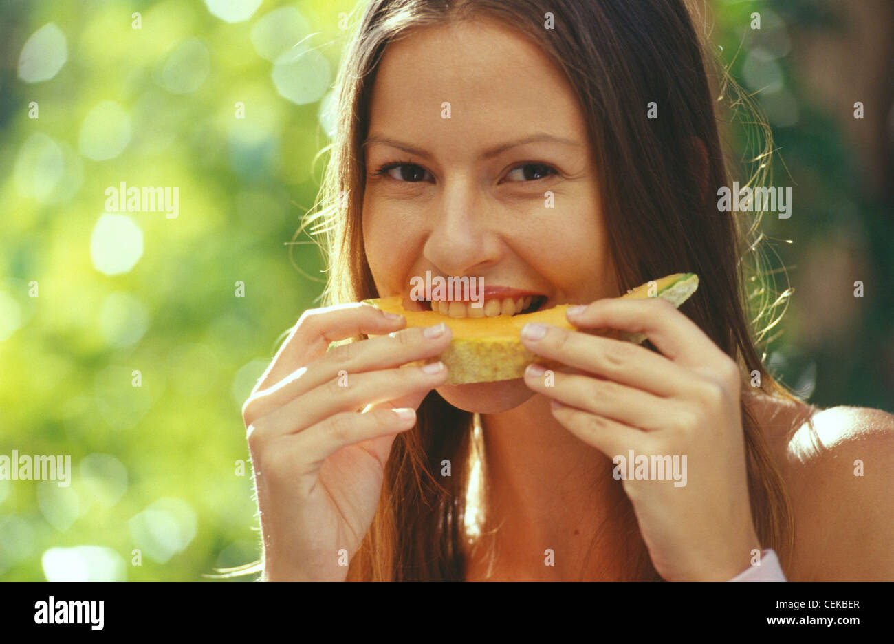 Brunette Female Straight Centre Parting Hair Eating Orange Honeydew Melon Both Hands In A 7949