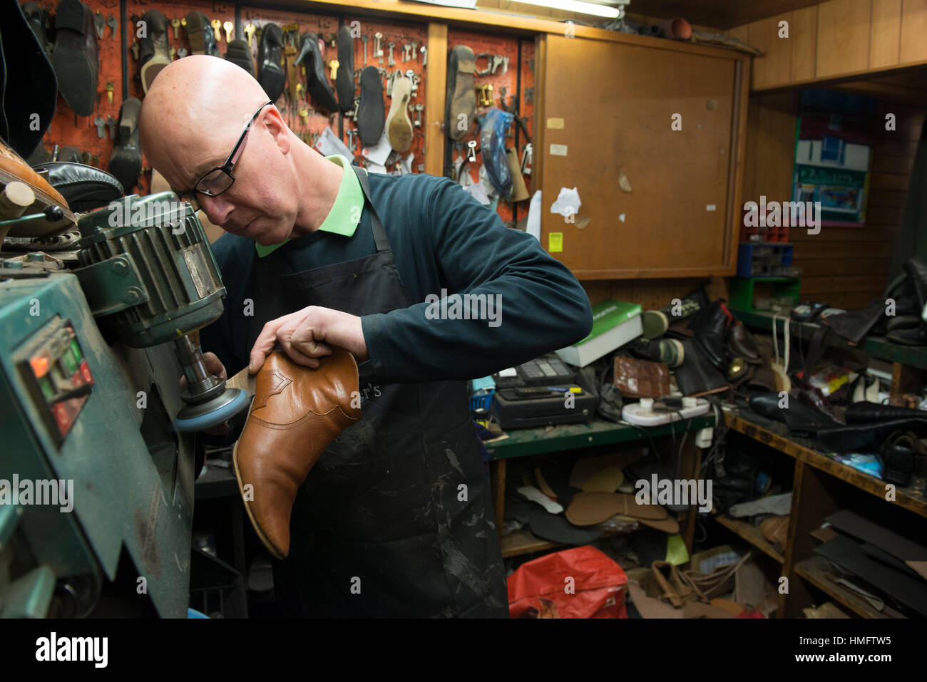 an old fashioned shoe repair / cobbler fixes shoes in his busy shop ...