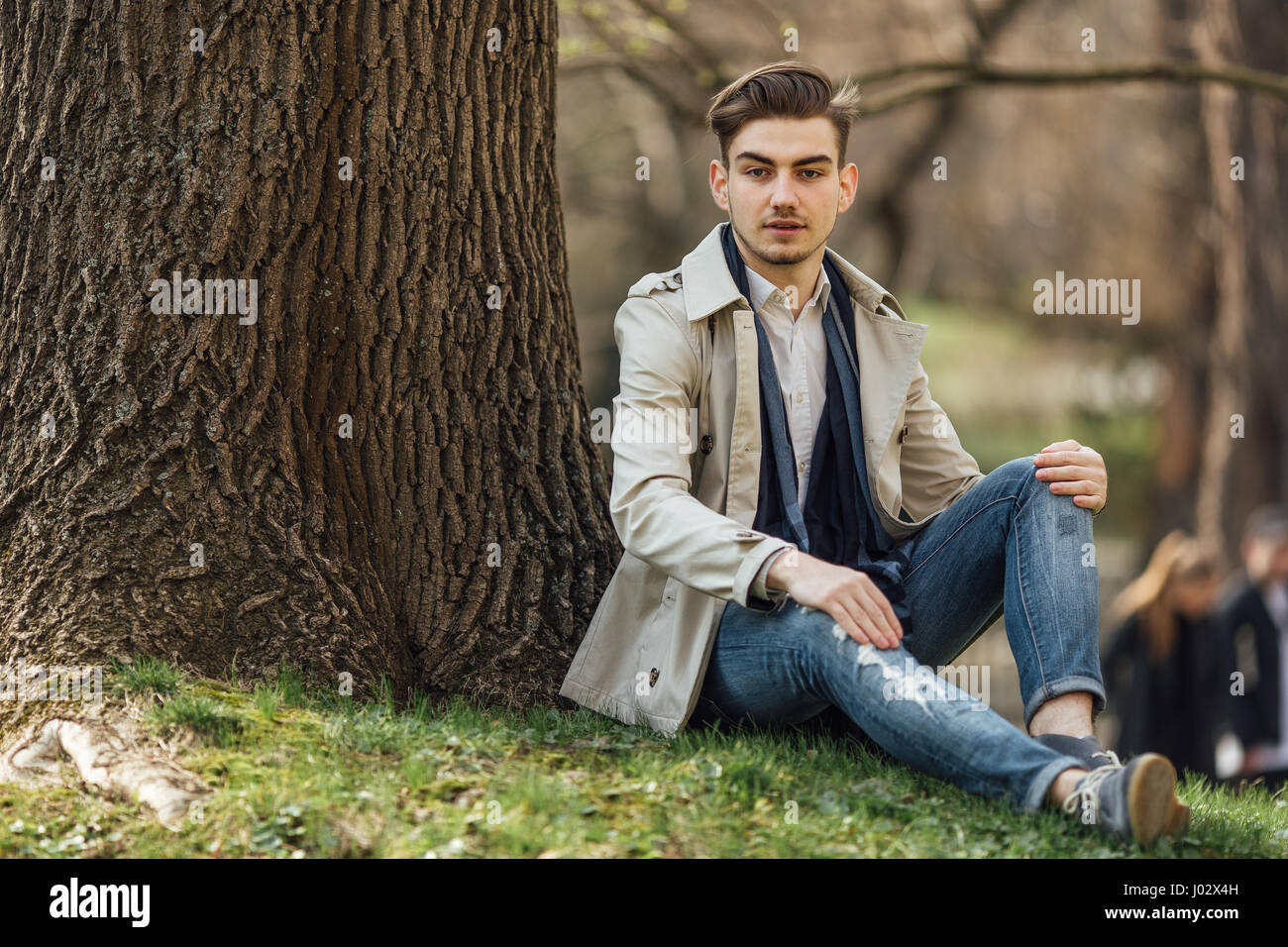 Fashionable man sitting near trees with blur background Stock Photo - Alamy