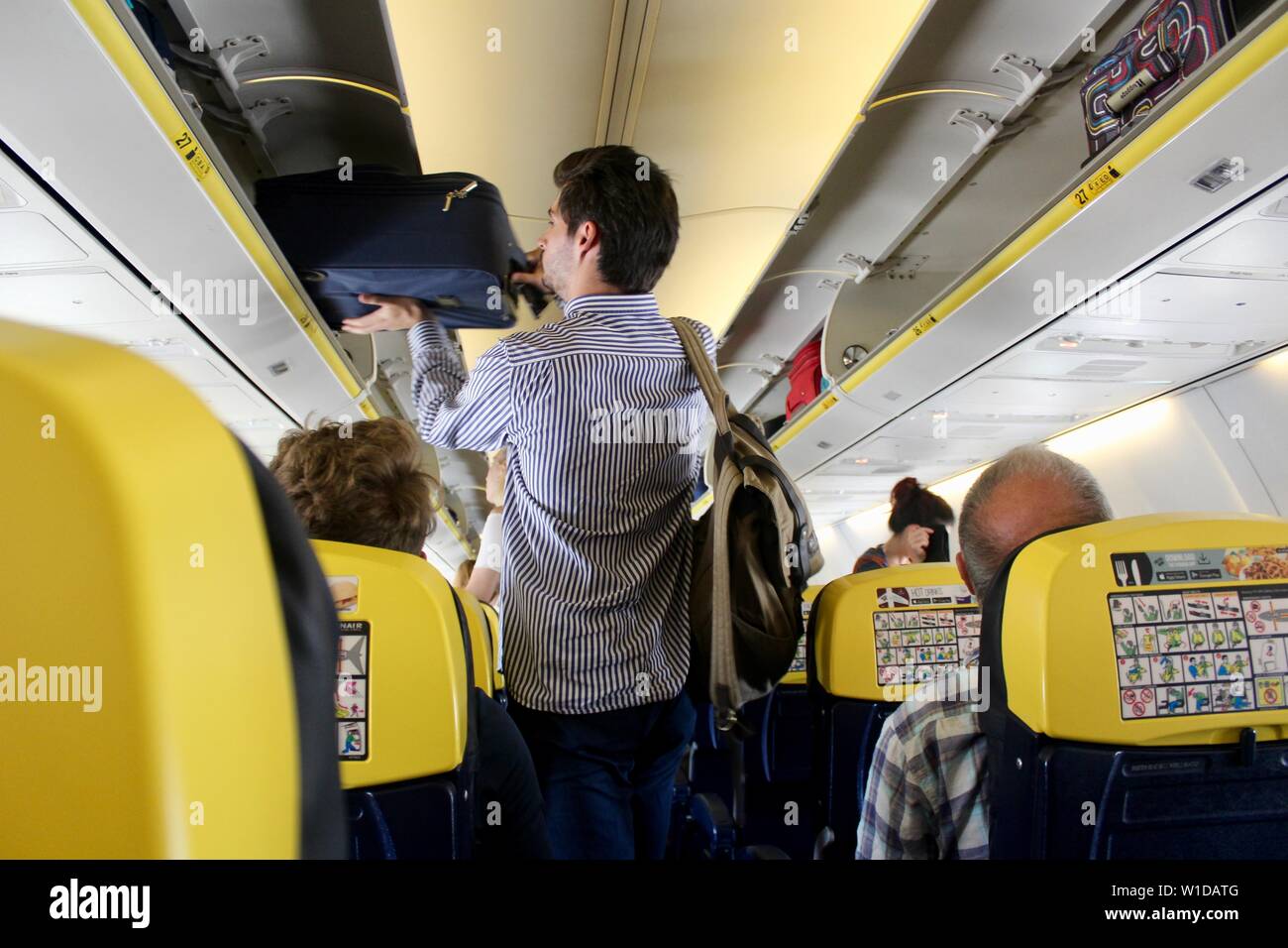 a man places his bag in an overhead locker on a ryanair flight Stock Photo - Alamy
