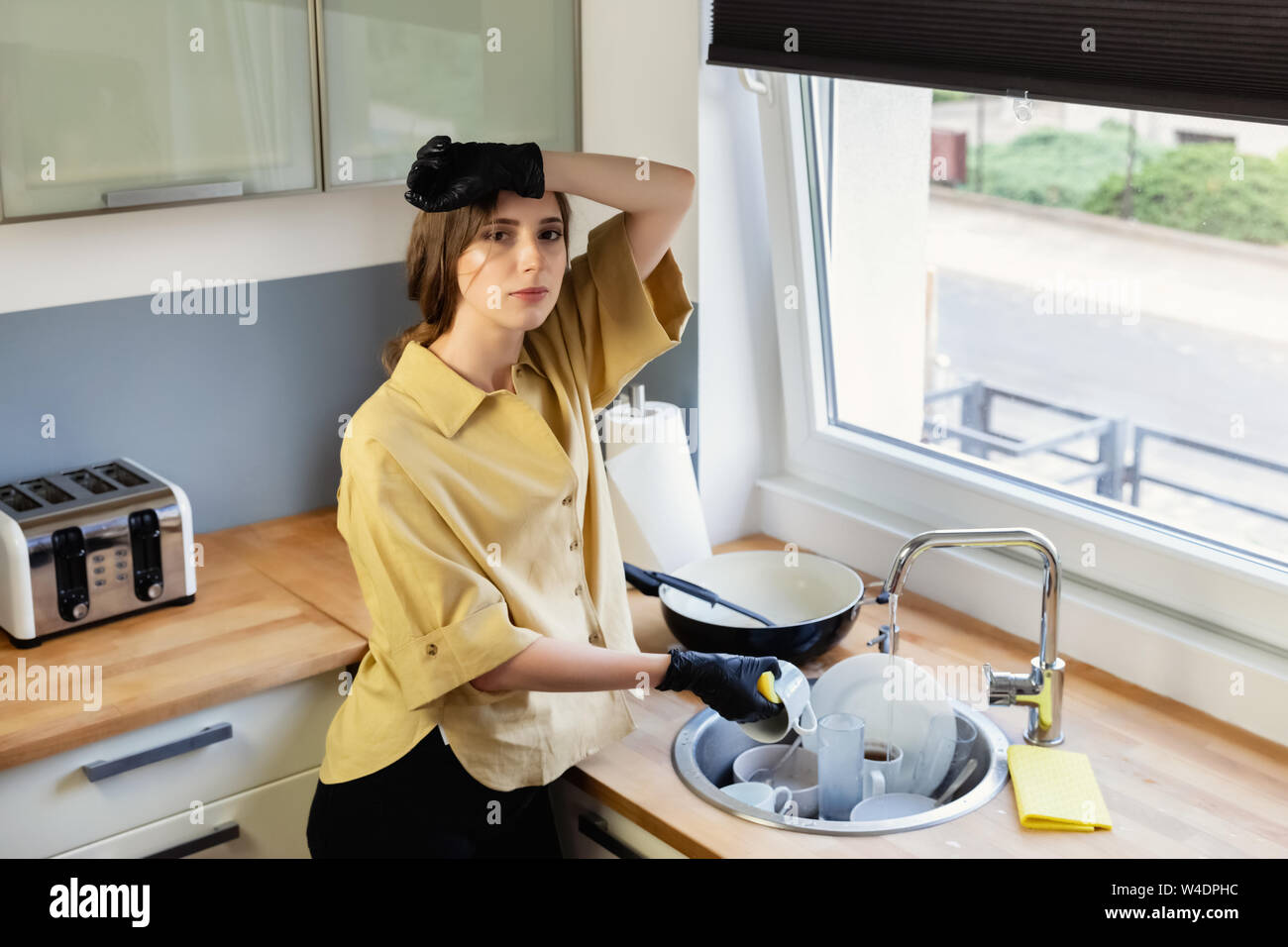 A Young Woman Cleans Up In The Kitchen Washing Dishes She Is Tired